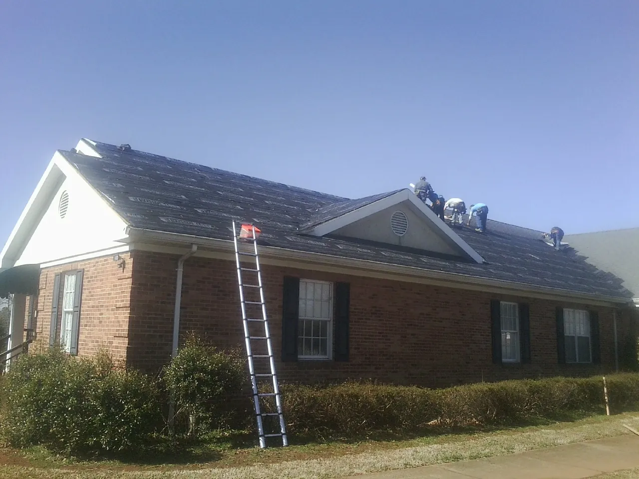 Crew tearing shingles off a brick ranch roof with a ladder set — Metal Roof Repair work by our crew in Keedysville