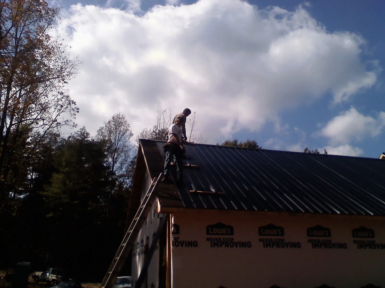 Roofer fastening dark metal panels high against a cloudy sky, from a Roof Inspection job in Keedysville