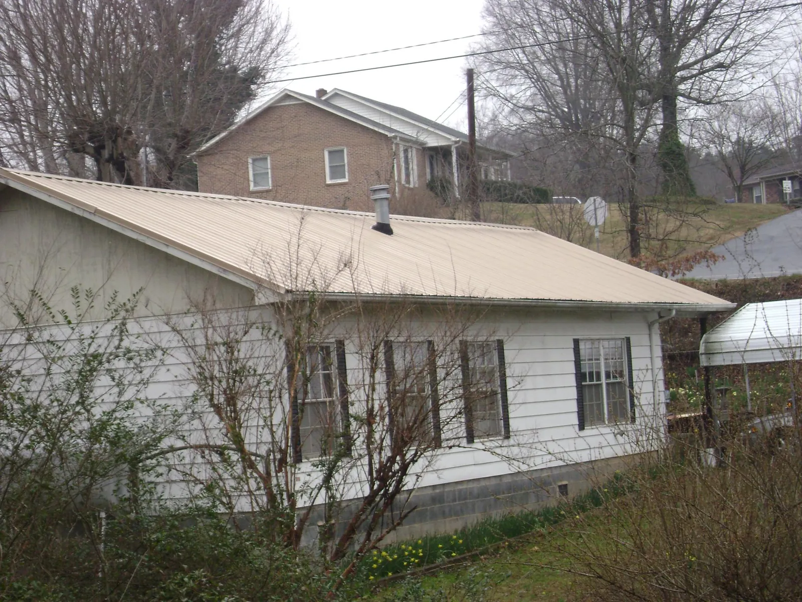 Tan metal roof on a white sided house set into a hillside — Commercial Roofing by Roofing Brothers in Keedysville